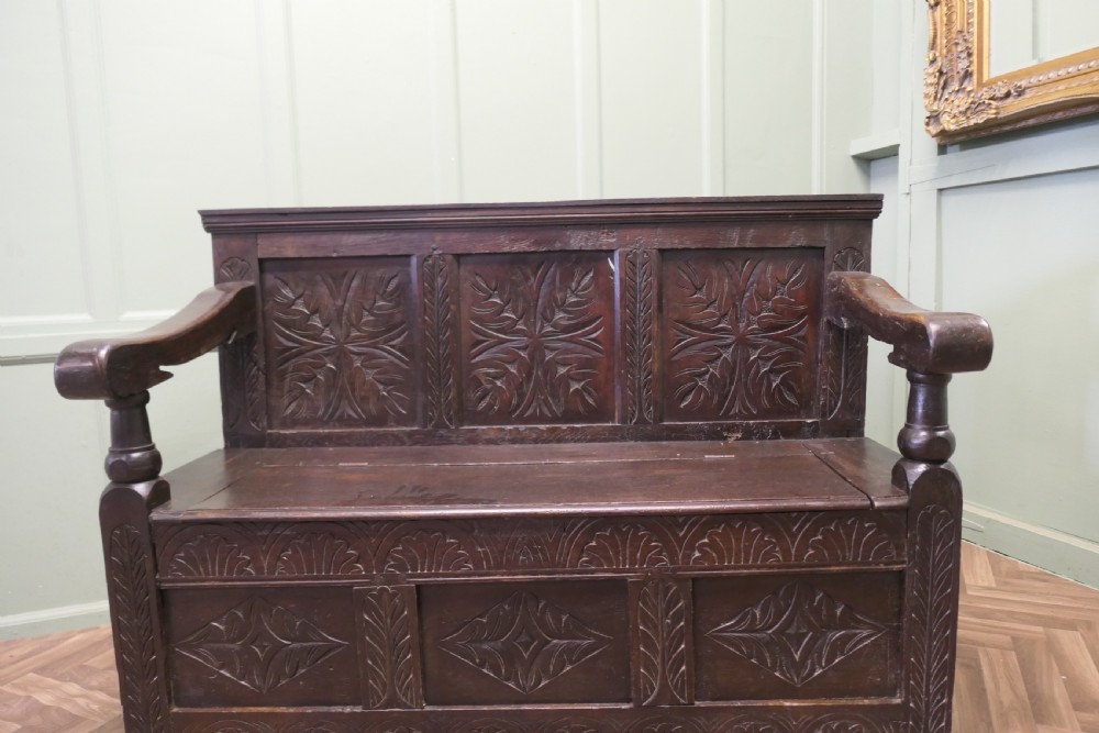 A dark carved oak high back box settle featuring three carved back panels, a hinged seat, and carved front base panels. View II