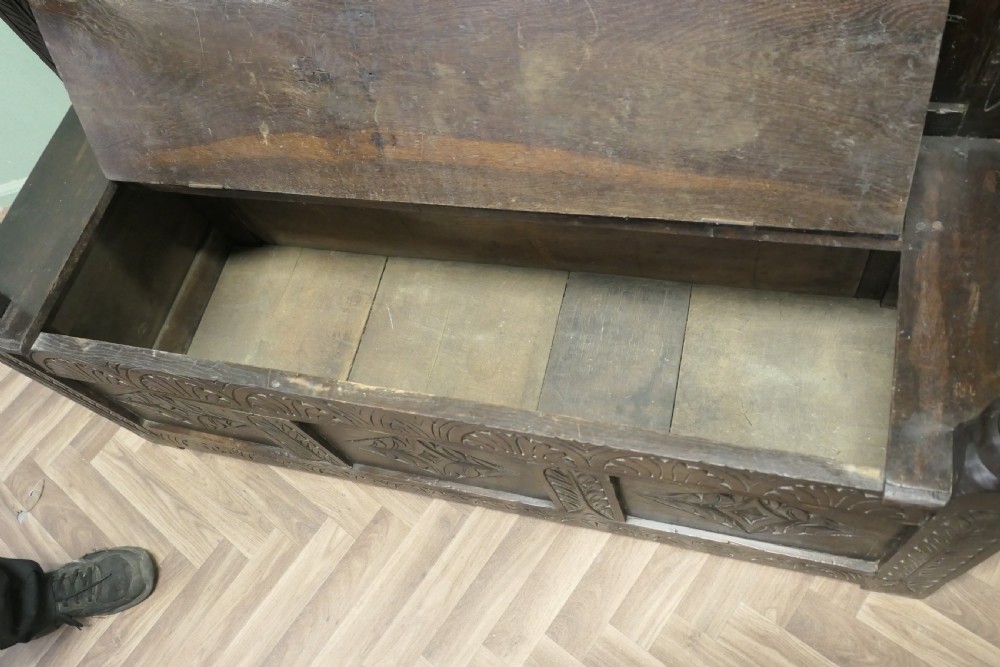 A dark carved oak high back box settle featuring three carved back panels, a hinged seat, and carved front base panels. View VII