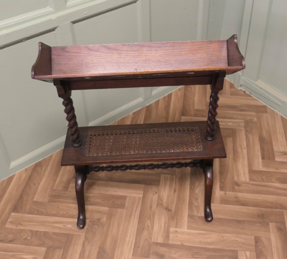 An oak book stand featuring a sloped upper shelf, barley twist supports, an woven cane lower shelf, and cabriole legs.