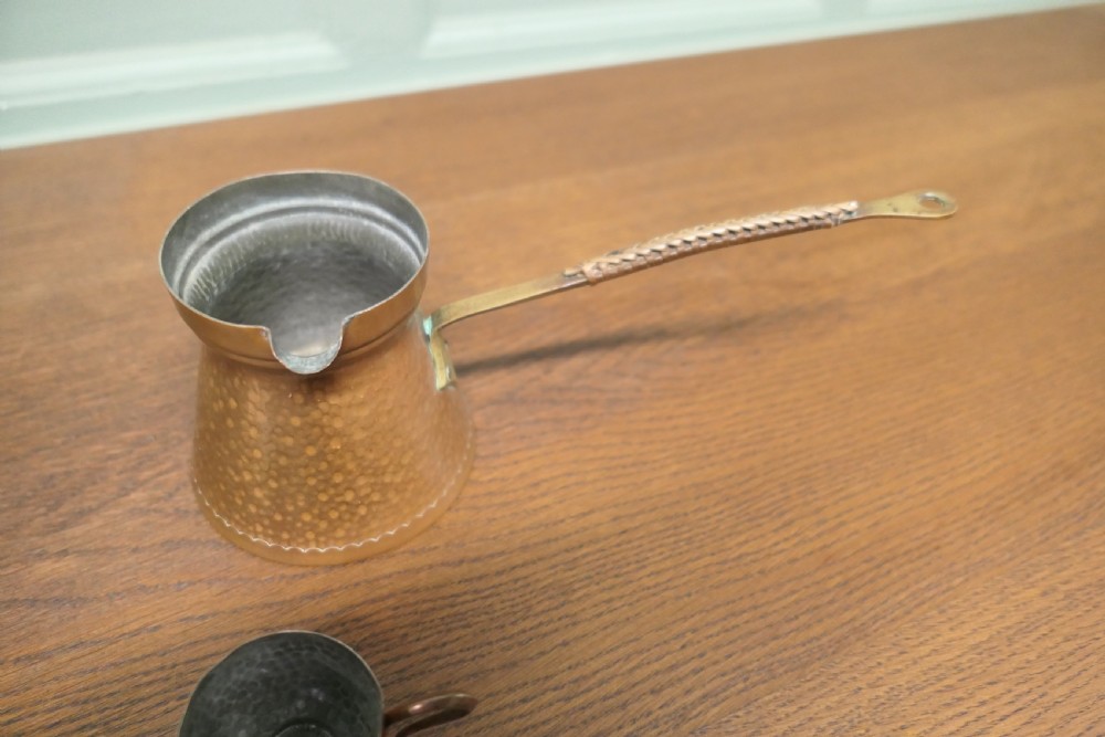 A hand-hammered copper pot featuring a long brass handle, pouring spout, and tin-lined interior.