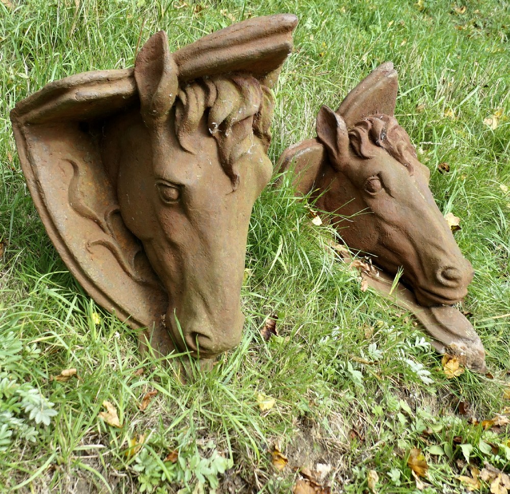 A pair of heavy cast iron wall brackets shaped as detailed horse heads with textured manes and integrated shelf support plates, displaying surface rust patina.