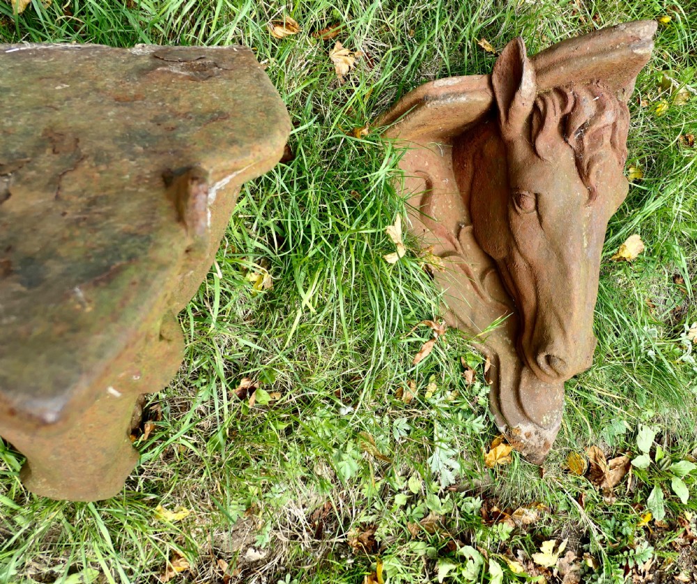 A pair of heavy cast iron wall brackets shaped as detailed horse heads with textured manes and integrated shelf support plates, displaying surface rust patina. View V