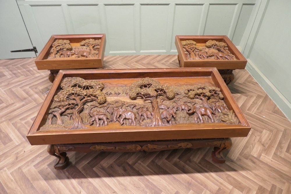 A three-piece teak table set featuring elaborate relief carvings of elephants amidst trees under glass tops. View II