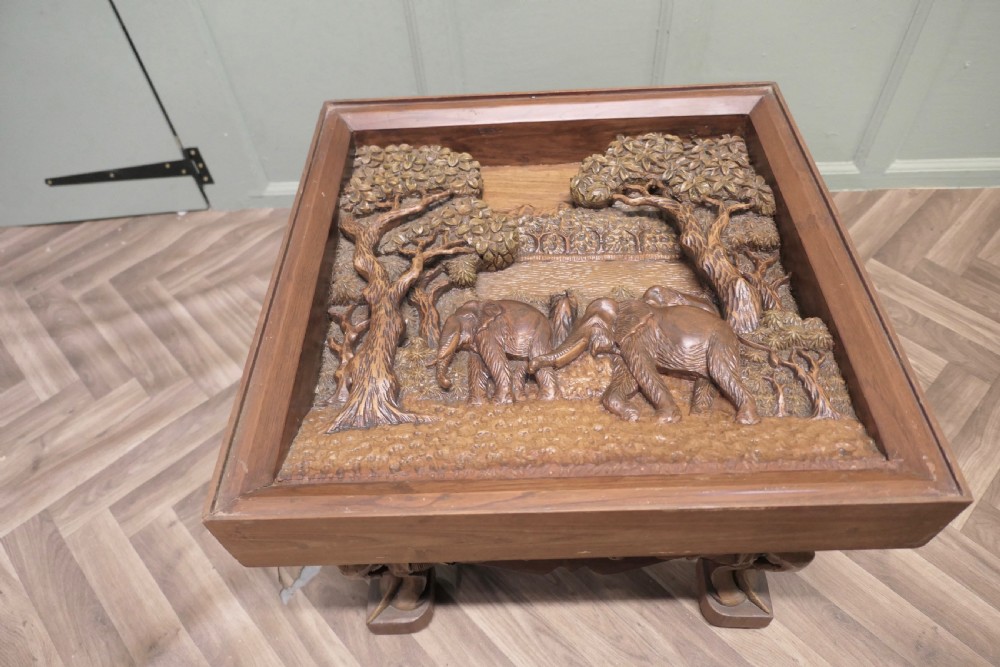 A three-piece teak table set featuring elaborate relief carvings of elephants amidst trees under glass tops. View V