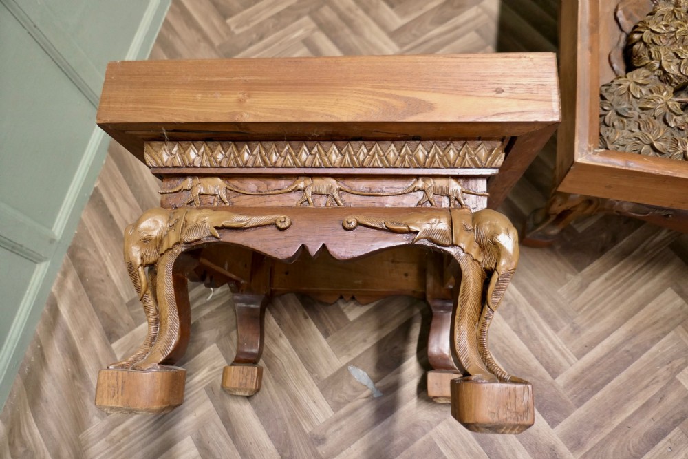 A three-piece teak table set featuring elaborate relief carvings of elephants amidst trees under glass tops. View VI