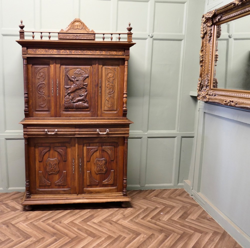 A two-tier carved oak French buffet de corps featuring a central high-relief panel depicting a hunting scene, spindled top gallery, and two-door lower base.