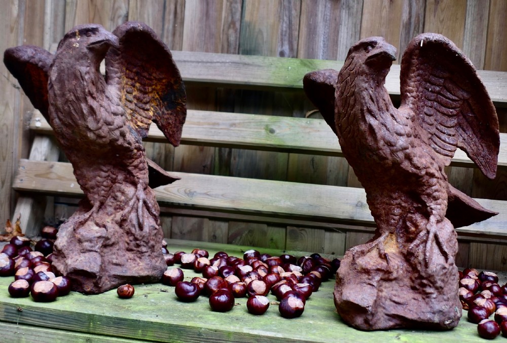 A pair of weathered cast iron eagle statues with outstretched wings perched on textured rock bases featuring a heavy rust patina.