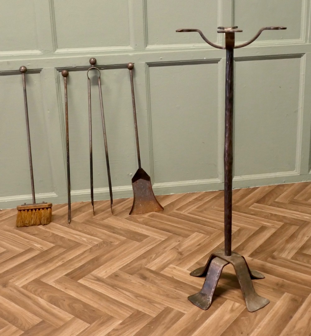 A dark hand-forged wrought iron fireplace companion set featuring a central stand with curved hooks holding a poker, shovel, tongs, and wooden brush. View V