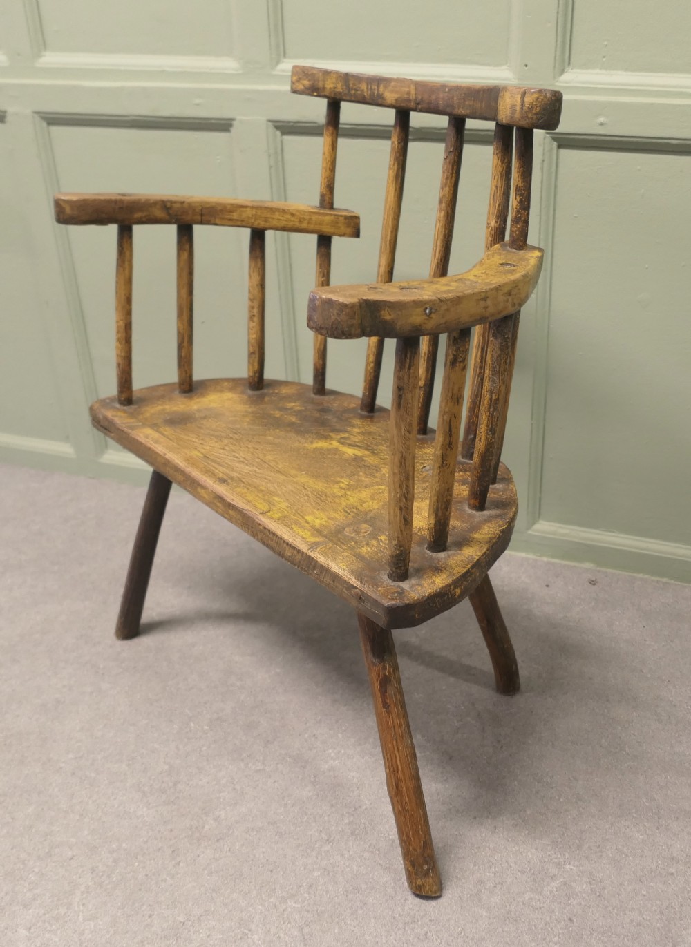 An 18th-century primitive wooden comb-back armchair featuring turned splayed legs, a thick shaped slab seat, and distressed yellow paint finish.