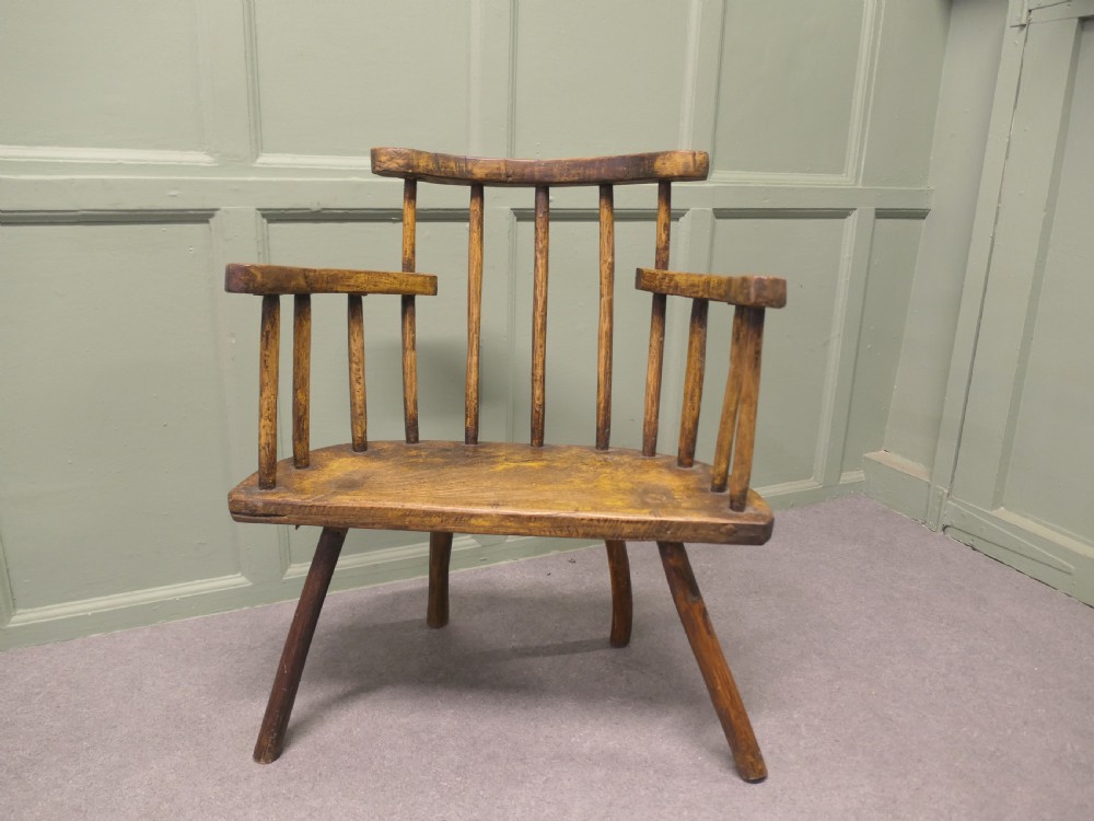 An 18th-century primitive wooden comb-back armchair featuring turned splayed legs, a thick shaped slab seat, and distressed yellow paint finish. View II