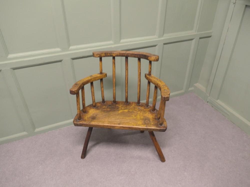 An 18th-century primitive wooden comb-back armchair featuring turned splayed legs, a thick shaped slab seat, and distressed yellow paint finish. View III