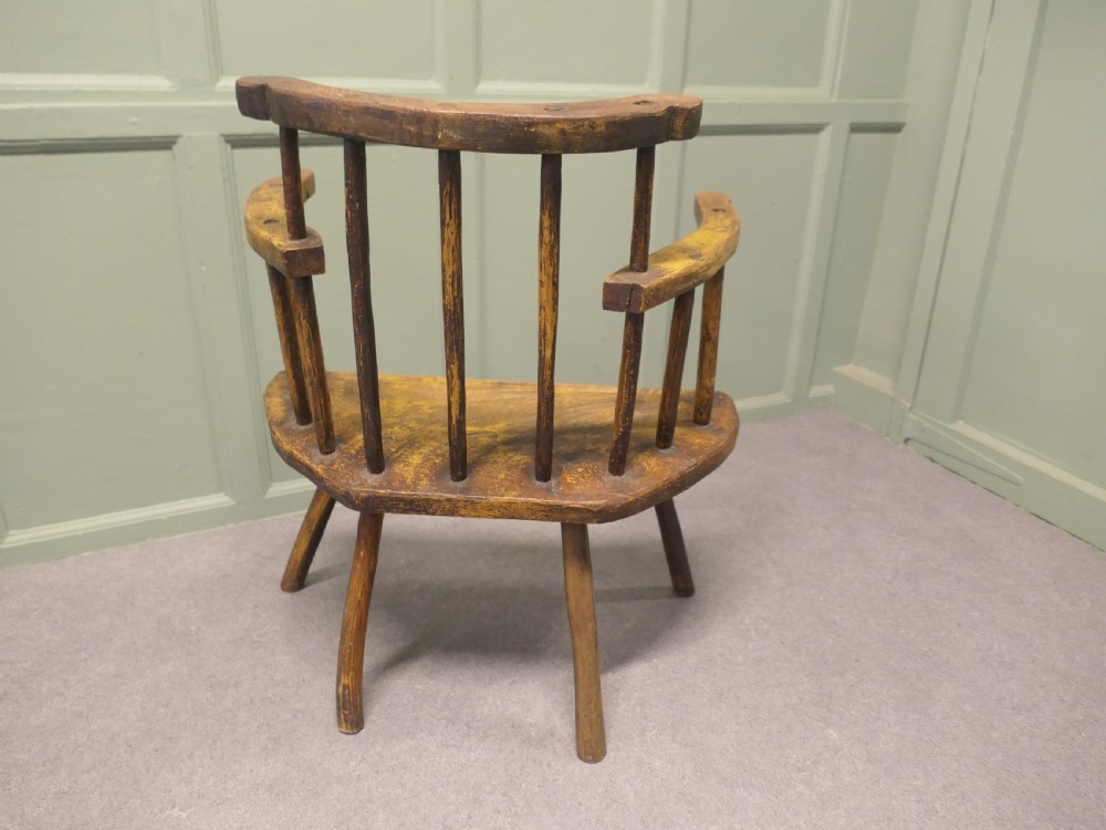 An 18th-century primitive wooden comb-back armchair featuring turned splayed legs, a thick shaped slab seat, and distressed yellow paint finish. View V