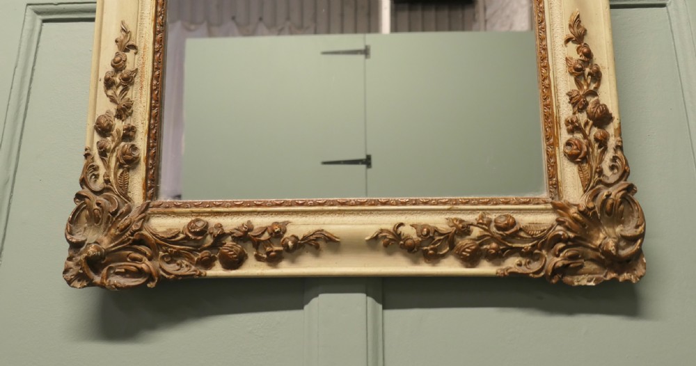 A rectangular French Rococo style wall mirror featuring a painted cream frame adorned with carved gilt floral and scroll ornamentation. View II