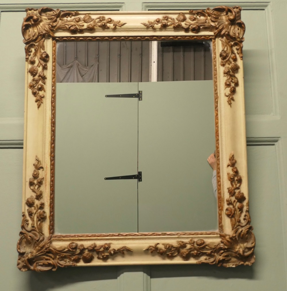 A rectangular French Rococo style wall mirror featuring a painted cream frame adorned with carved gilt floral and scroll ornamentation. View III