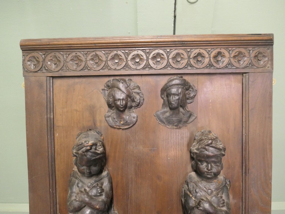 A pair of moulded dark brown leathermache putti term figures with arms crossed, mounted vertically on a timber panel. View IV