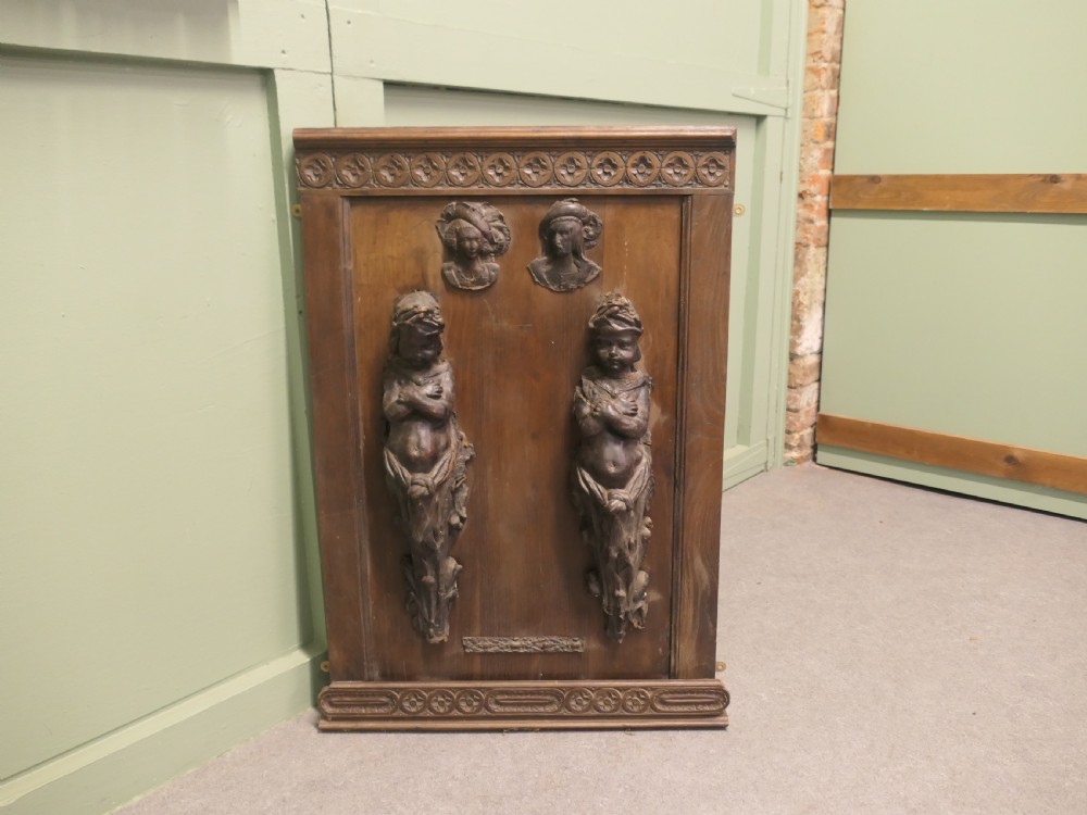 A pair of moulded dark brown leathermache putti term figures with arms crossed, mounted vertically on a timber panel. View VI