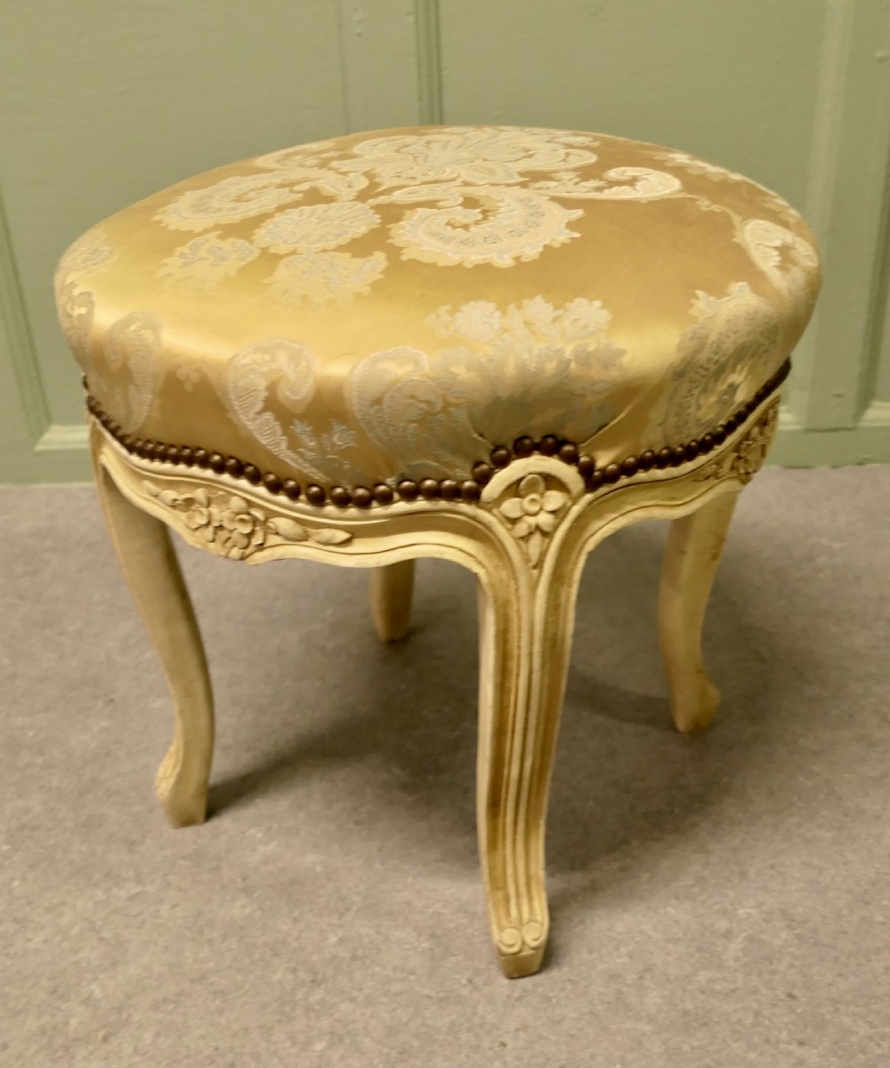 A circular French-style upholstered boudoir stool featuring cream painted cabriole legs with carved floral apron details, brass stud trim, and gold damask upholstery. View IV