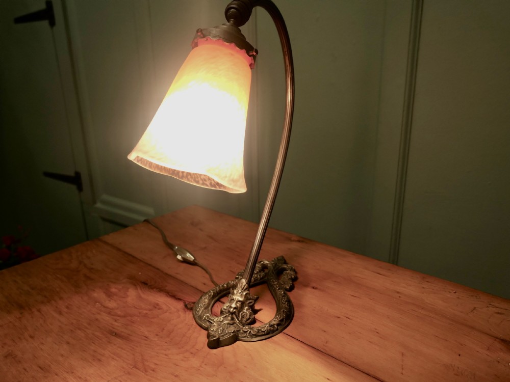 A French cast brass desk lamp featuring a curved gooseneck arm, an openwork base with a Bacchus face motif, and a flared frosted glass shade with an orange to pale pink gradient. View II
