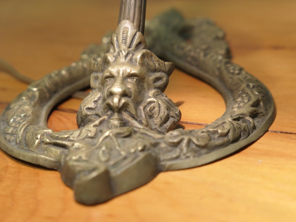 A French cast brass desk lamp featuring a curved gooseneck arm, an openwork base with a Bacchus face motif, and a flared frosted glass shade with an orange to pale pink gradient. View III