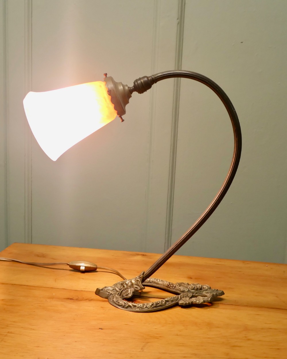 A French cast brass desk lamp featuring a curved gooseneck arm, an openwork base with a Bacchus face motif, and a flared frosted glass shade with an orange to pale pink gradient. View VI