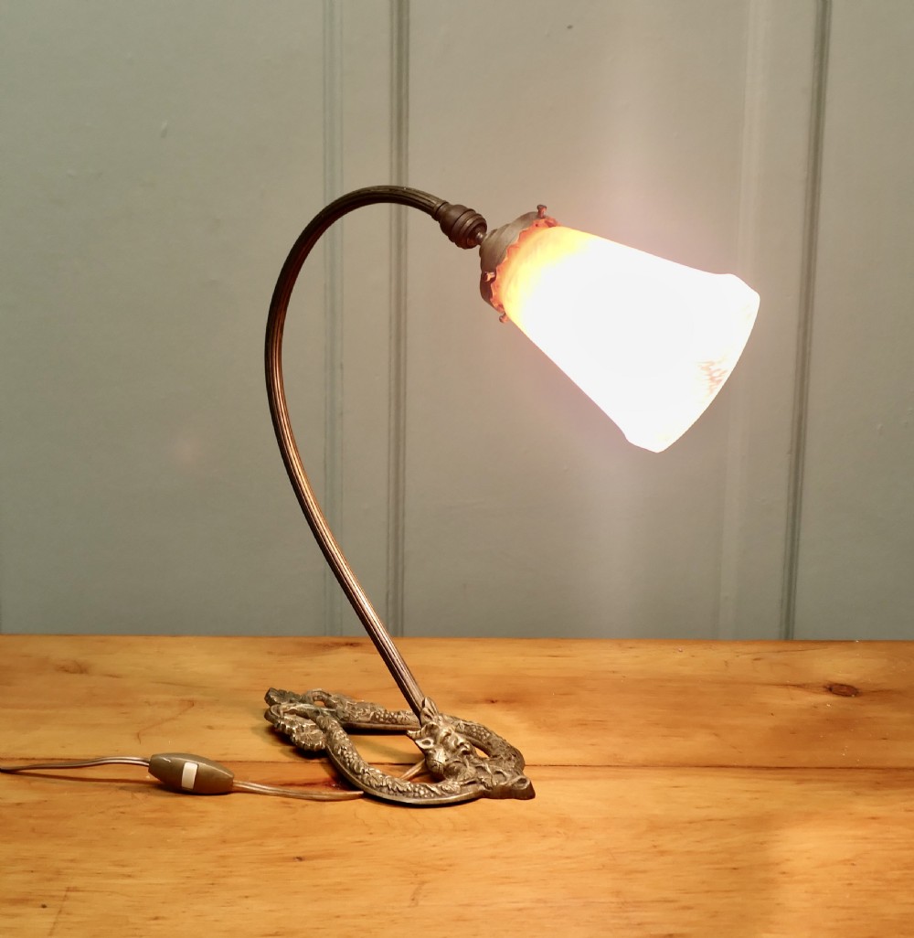 A French cast brass desk lamp featuring a curved gooseneck arm, an openwork base with a Bacchus face motif, and a flared frosted glass shade with an orange to pale pink gradient. View VII