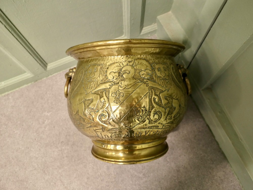 A nineteenth-century embossed brass jardiniere featuring heraldic lion motifs, a shield crest, lion head side handles, and a stepped pedestal base.