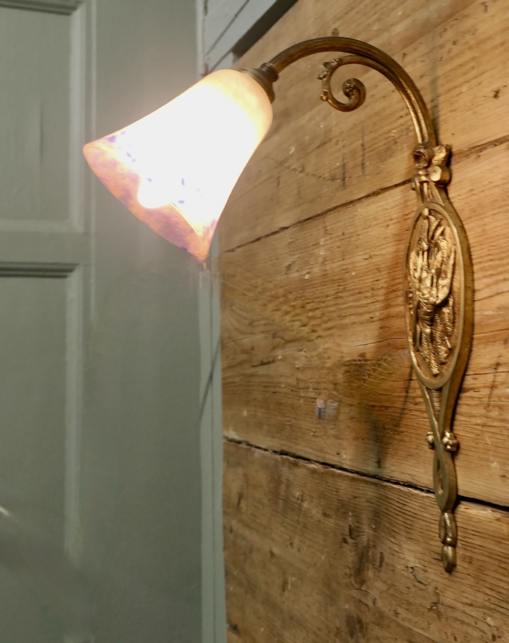 A French cast brass wall light featuring a decorative backplate, curved gooseneck arm, and bell-shaped mottled glass shade.