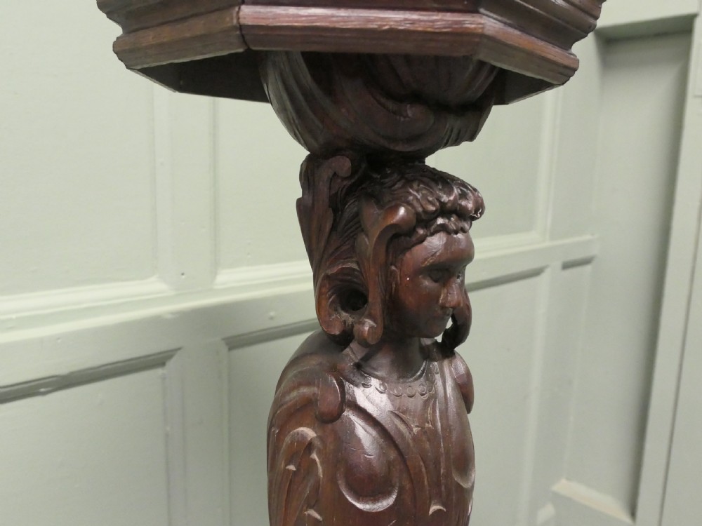 A dark carved oak pedestal featuring a caryatid figure and relief serpent design supporting an octagonal top platform. View II