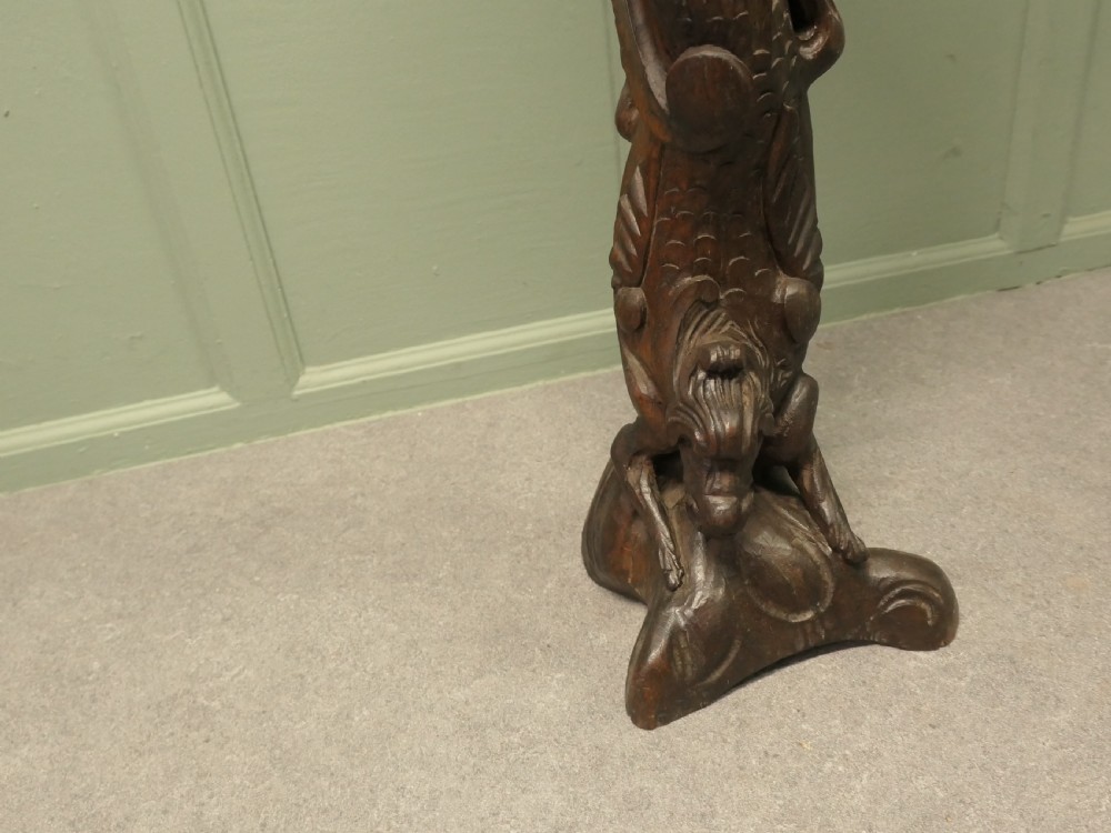 A dark carved oak pedestal featuring a caryatid figure and relief serpent design supporting an octagonal top platform. View III