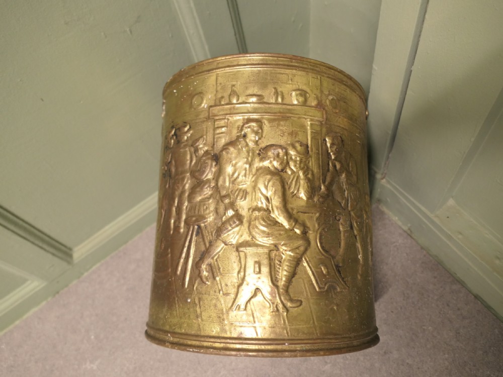 A cylindrical brass coal bucket featuring embossed tavern scenes in relief and a curved swing handle. View II