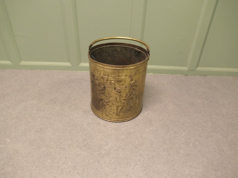 A cylindrical brass coal bucket featuring embossed tavern scenes in relief and a curved swing handle. View V