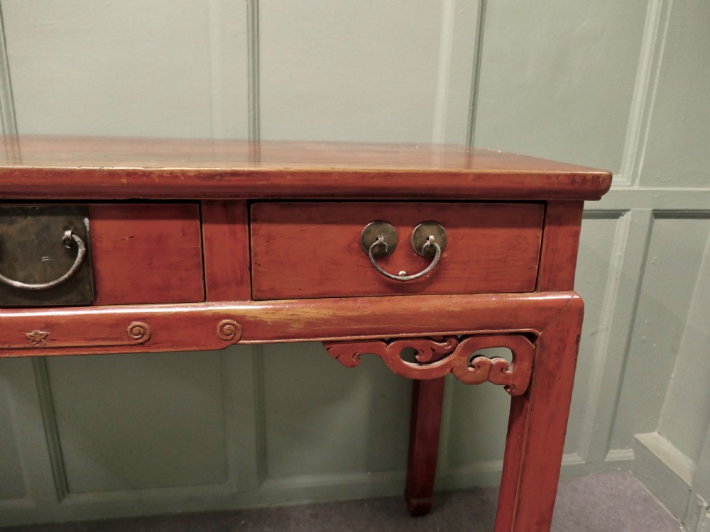 A red lacquered timber console table featuring three drawers with brass drop handles and carved corner spandrels over straight square legs. View II