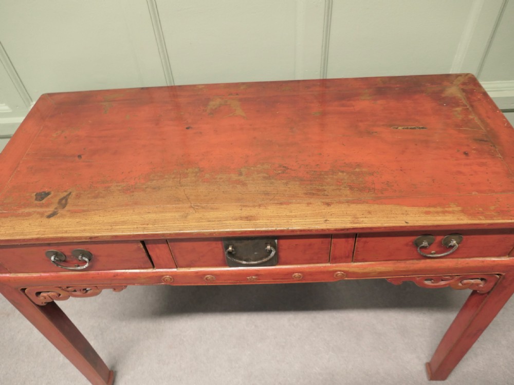 A red lacquered timber console table featuring three drawers with brass drop handles and carved corner spandrels over straight square legs. View III