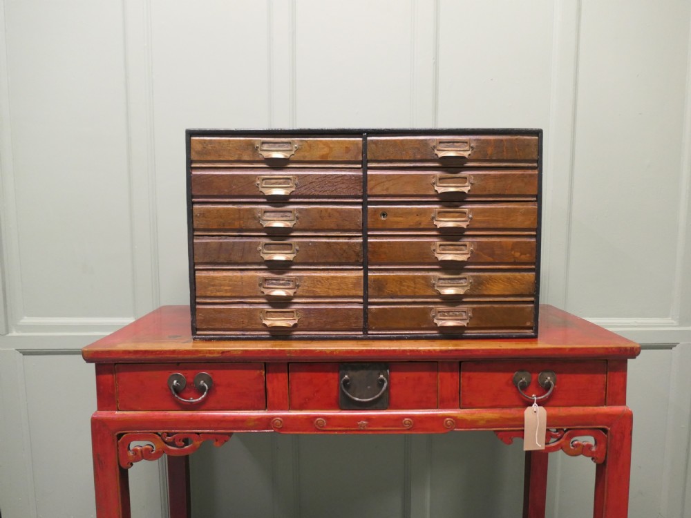 A desktop oak cabinet featuring twelve shallow drawers arranged in two columns, fitted with brass cup handles and label holders. View III