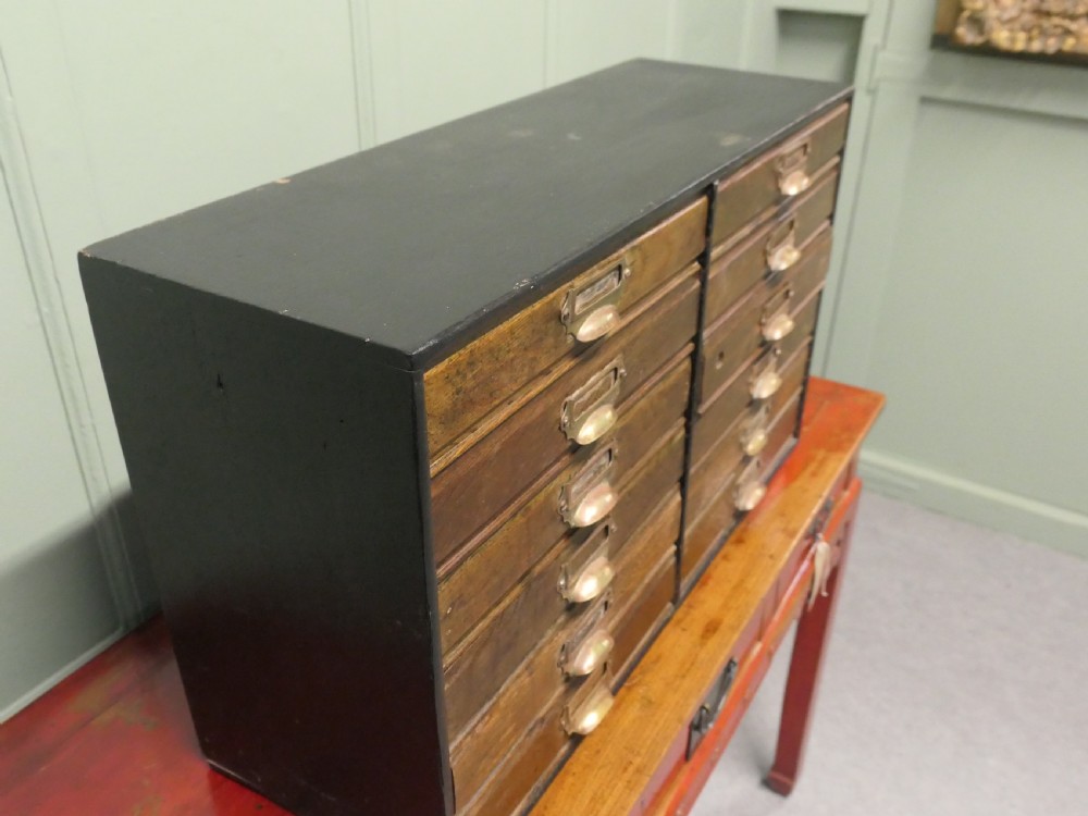 A desktop oak cabinet featuring twelve shallow drawers arranged in two columns, fitted with brass cup handles and label holders. View VI