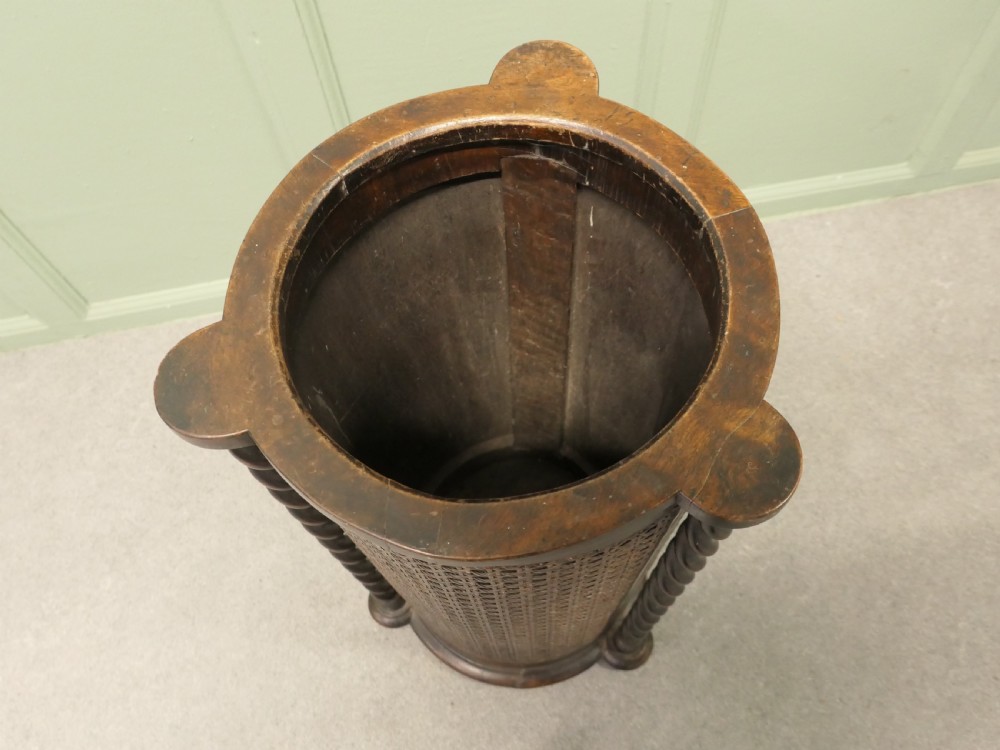 A dark brown cylindrical wooden stick stand featuring woven bergere panels and vertical barley twist supports. View V