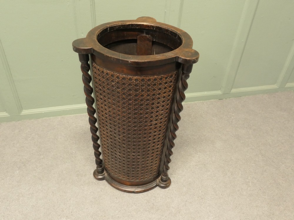 A dark brown cylindrical wooden stick stand featuring woven bergere panels and vertical barley twist supports. View VI