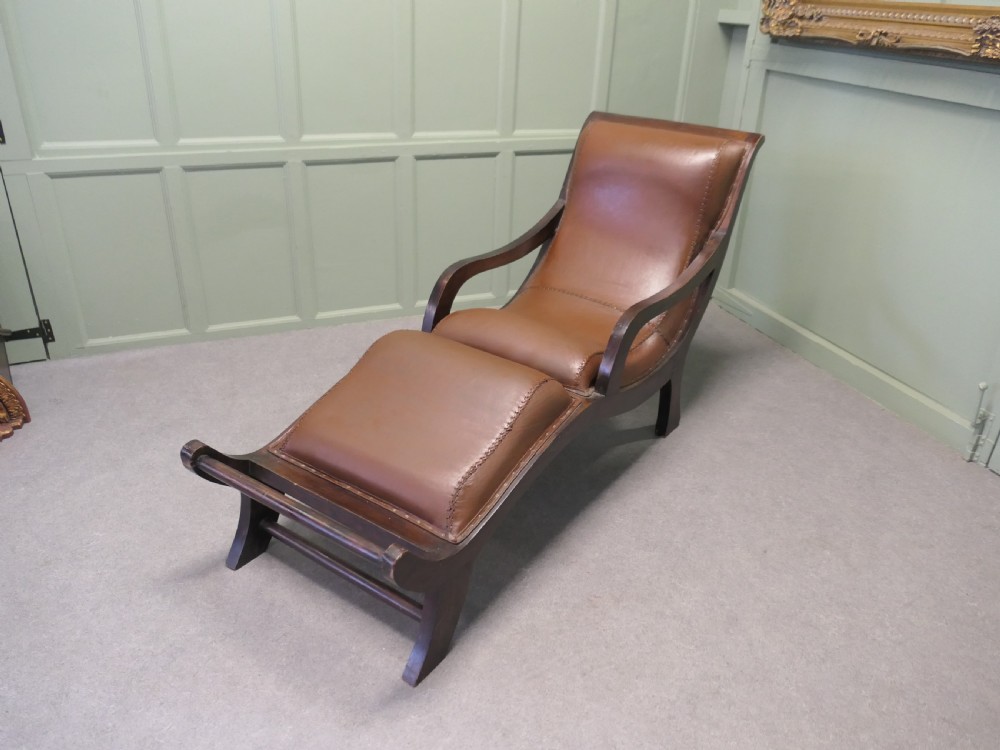A Victorian colonial plantation chaise longue featuring a curved mahogany frame, extended arms, and rich brown leather upholstery with metal stud detailing. View II