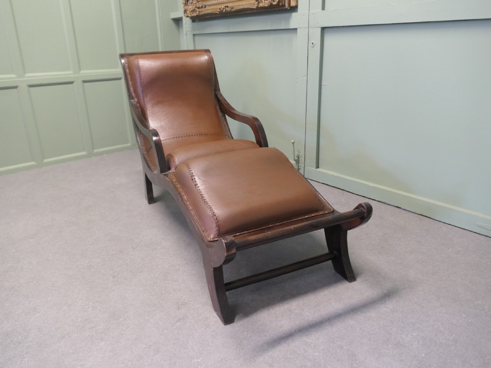 A Victorian colonial plantation chaise longue featuring a curved mahogany frame, extended arms, and rich brown leather upholstery with metal stud detailing. View III