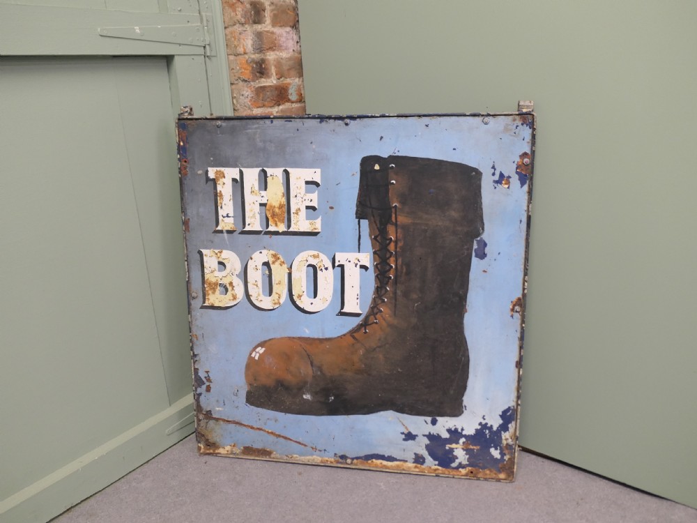 A square weathered painted iron pub sign depicting a brown boot alongside white text reading THE BOOT against a light blue background.