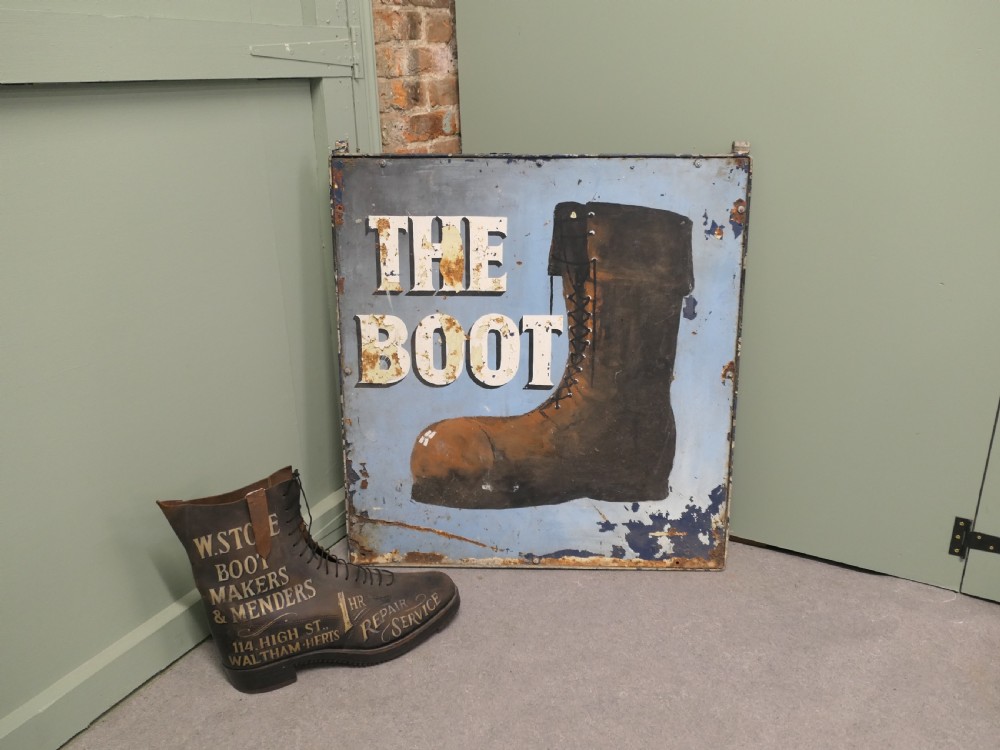 A square weathered painted iron pub sign depicting a brown boot alongside white text reading THE BOOT against a light blue background. View II