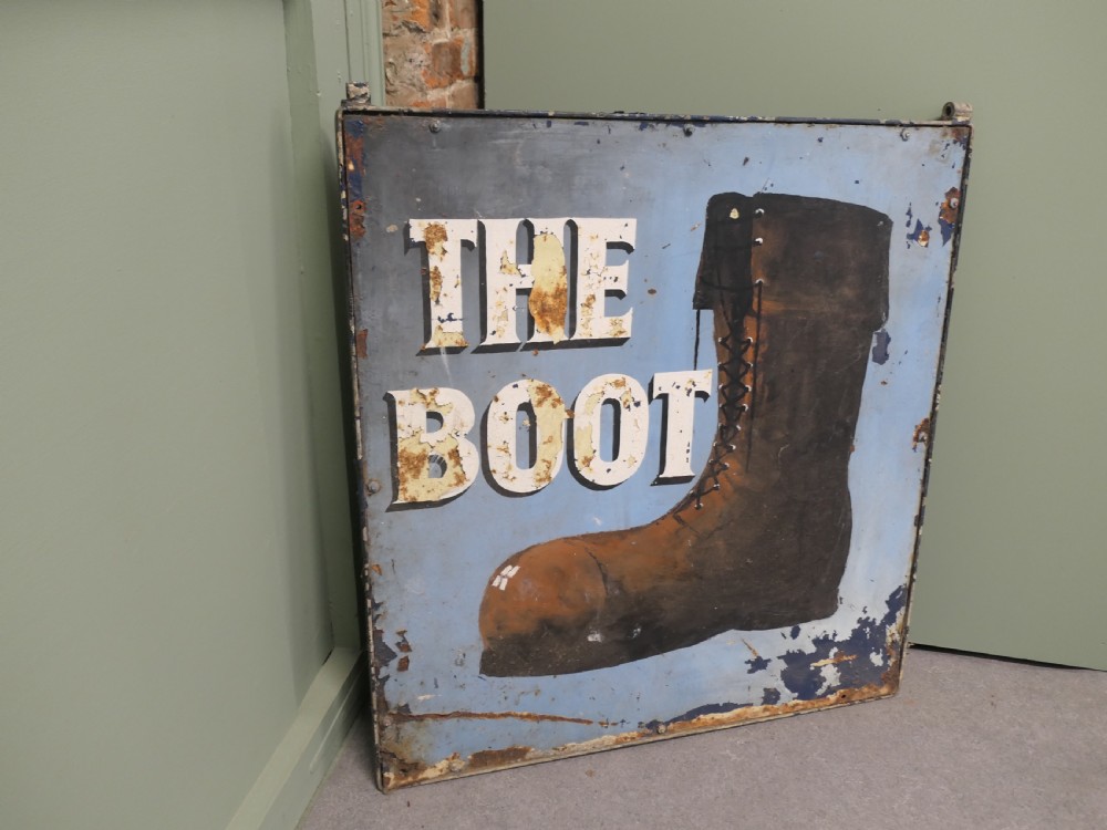 A square weathered painted iron pub sign depicting a brown boot alongside white text reading THE BOOT against a light blue background. View VI