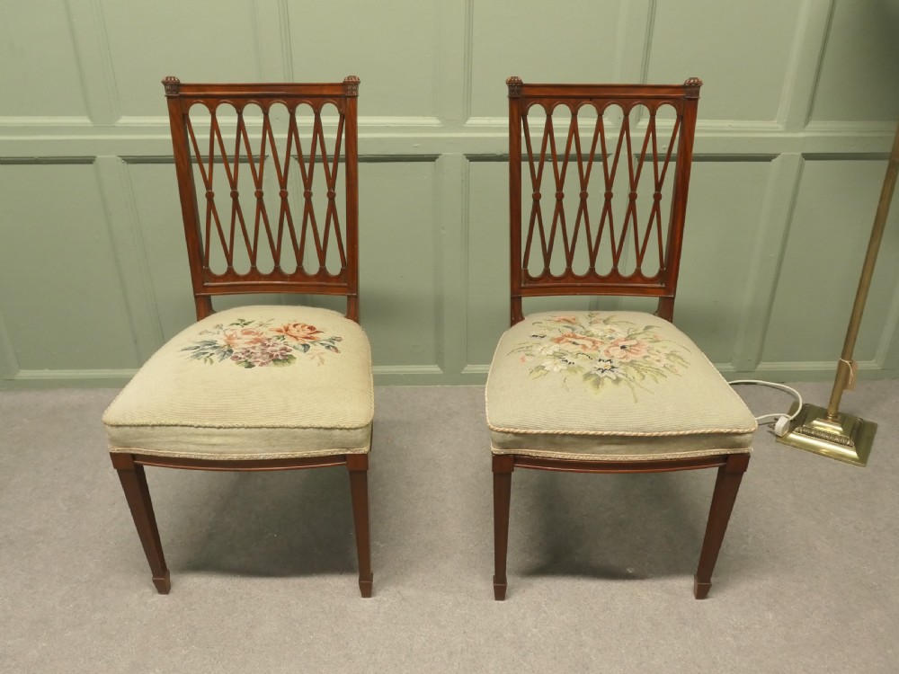 A pair of antique walnut hall chairs with lattice openwork backs and floral needlepoint upholstered seats.