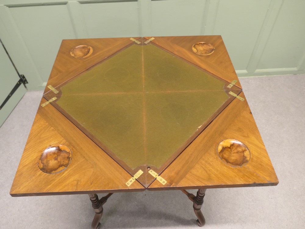 A late Victorian mahogany envelope card table with four triangular flaps unfolding to reveal a central green baize surface and four circular counter wells. View II