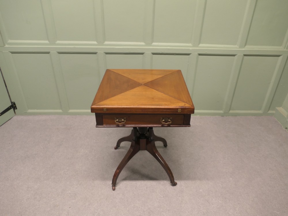 A Victorian mahogany envelope card table featuring four triangular folding top leaves, a single drawer with brass handles, and a turned central pedestal on four splayed legs with castors.