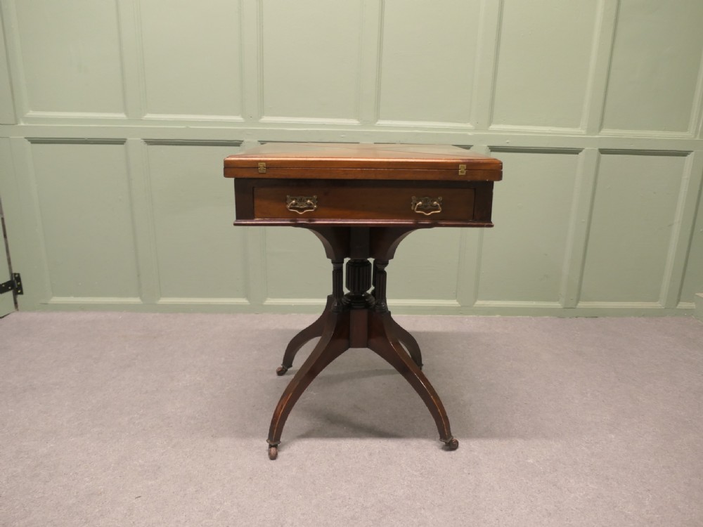 A Victorian mahogany envelope card table featuring four triangular folding top leaves, a single drawer with brass handles, and a turned central pedestal on four splayed legs with castors. View II