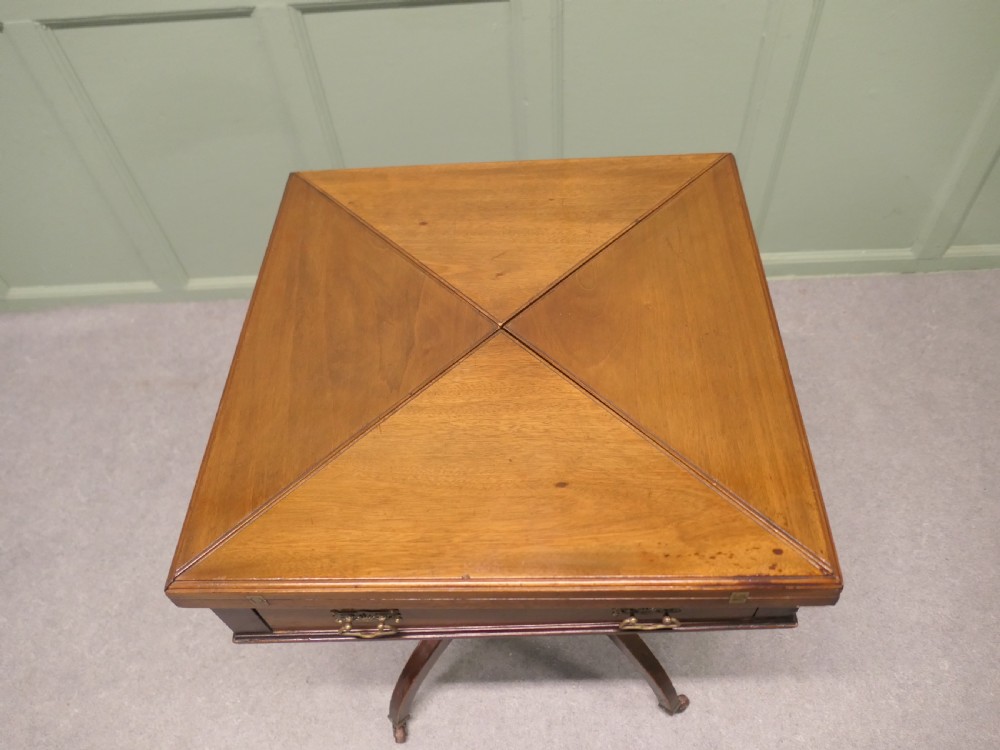 A Victorian mahogany envelope card table featuring four triangular folding top leaves, a single drawer with brass handles, and a turned central pedestal on four splayed legs with castors. View V