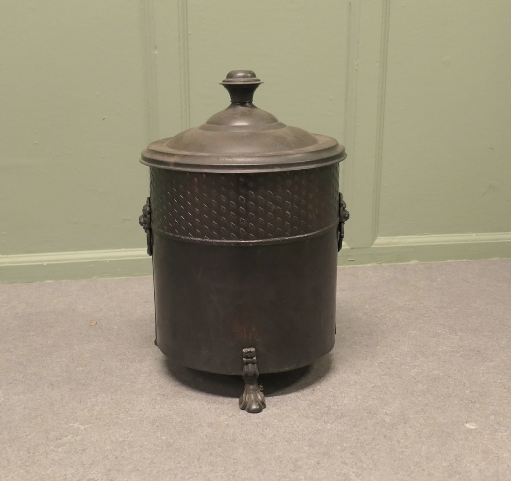 A dark patinated metal cylindrical coal bucket featuring a stepped lidded top with an urn finial, a diamond lattice pattern band, side handles, and cast feet.