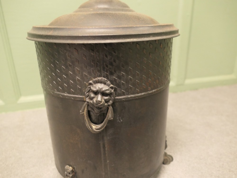 A dark patinated metal cylindrical coal bucket featuring a stepped lidded top with an urn finial, a diamond lattice pattern band, side handles, and cast feet. View II