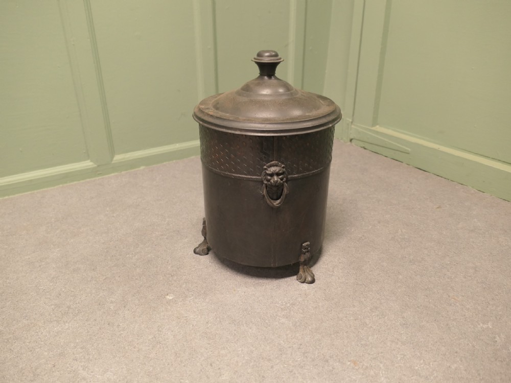A dark patinated metal cylindrical coal bucket featuring a stepped lidded top with an urn finial, a diamond lattice pattern band, side handles, and cast feet. View V